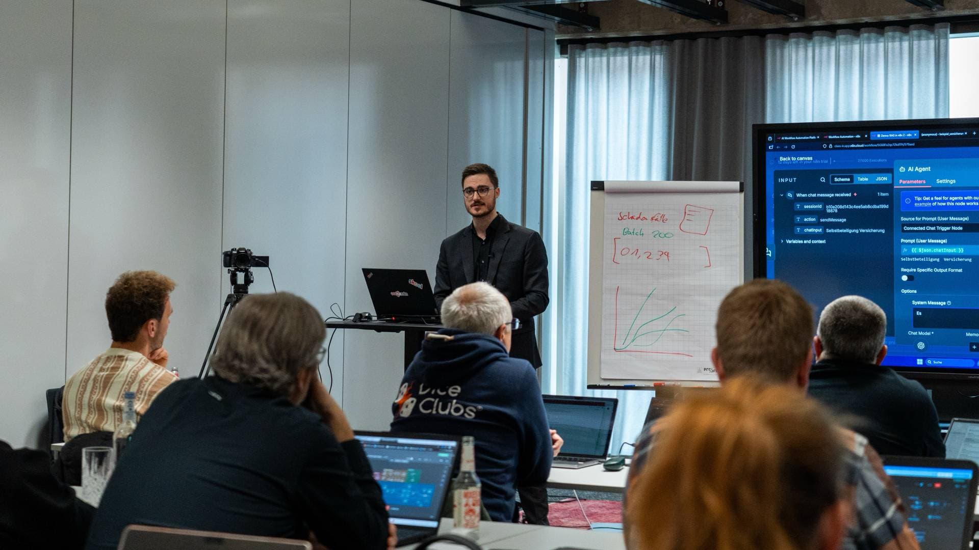 Workshop-Situation: Vor einer Gruppe an Laptops wird ein KI-Workflow am Bildschirm und am Flipchart erklärt